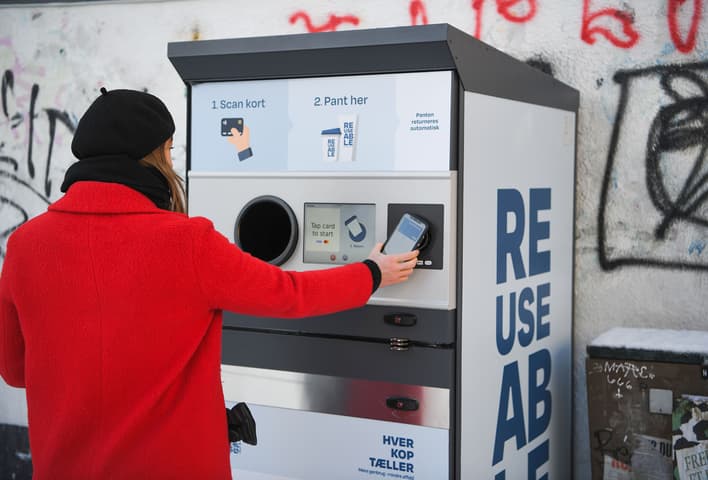 Danimarka'nın Aarhus şehrindeki bir TOMRA toplama noktasında, yeniden kullanılabilir bir bardağı iade eden tüketici